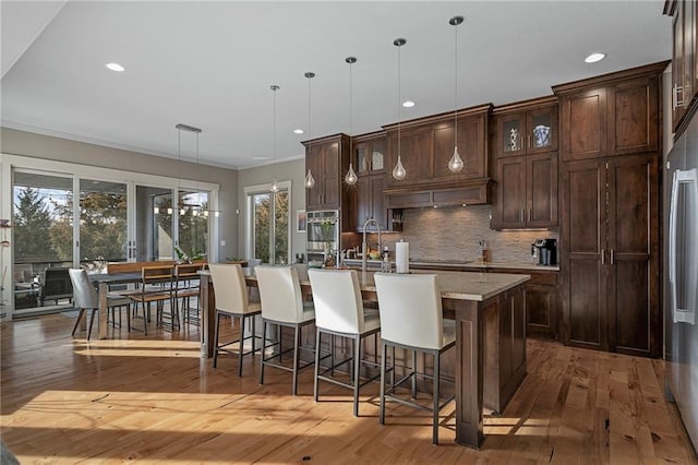 kitchen with tasteful backsplash, a center island with sink, hardwood / wood-style floors, stainless steel oven, and pendant lighting