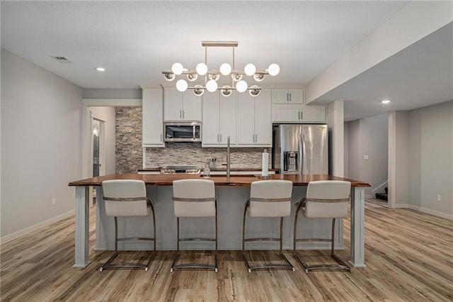 kitchen with butcher block countertops, visible vents, appliances with stainless steel finishes, backsplash, and a center island with sink