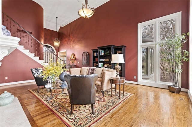 living area featuring a towering ceiling, baseboards, stairway, and wood finished floors