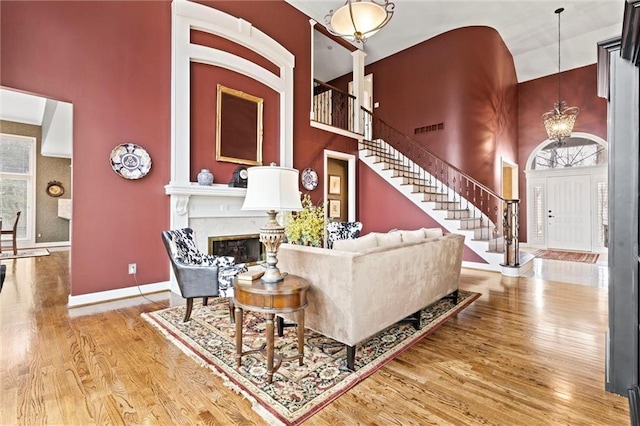 living area with a fireplace, visible vents, stairway, a towering ceiling, and wood finished floors