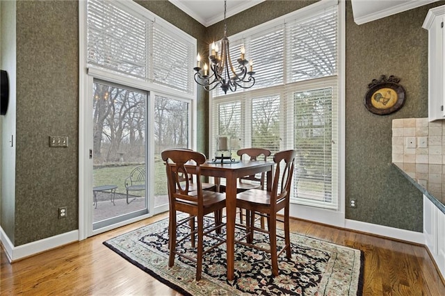 dining area featuring a notable chandelier, wood finished floors, baseboards, wallpapered walls, and crown molding