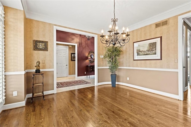 unfurnished dining area featuring a notable chandelier, visible vents, ornamental molding, wood finished floors, and baseboards