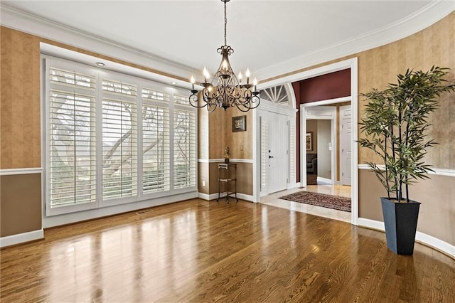 unfurnished dining area with ornamental molding, a chandelier, baseboards, and wood finished floors