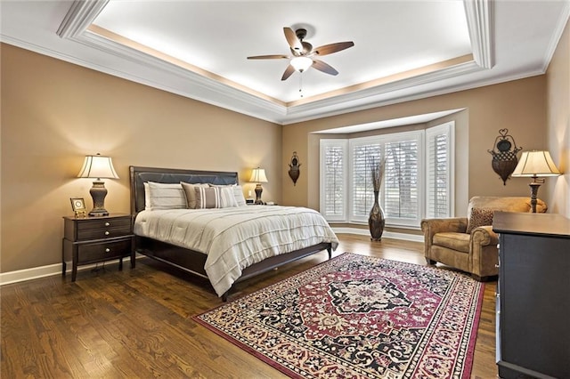 bedroom with dark wood-style floors, a tray ceiling, ornamental molding, a ceiling fan, and baseboards