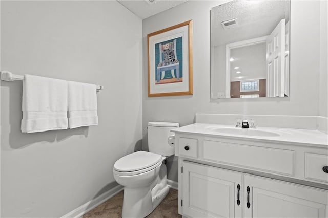 half bath with toilet, vanity, visible vents, and baseboards