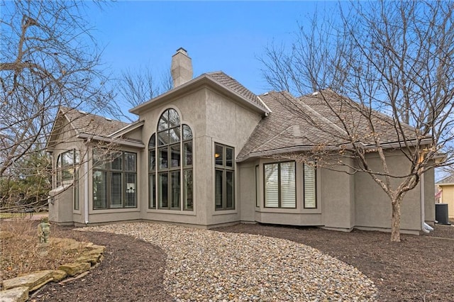 back of property with central air condition unit, a chimney, and stucco siding