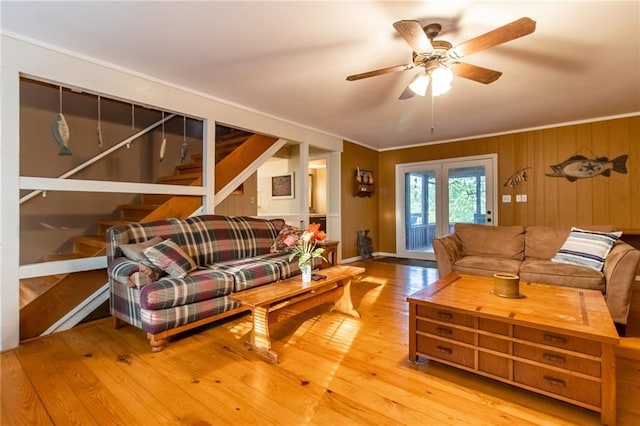 living room with ceiling fan, crown molding, light wood-type flooring, and wood walls