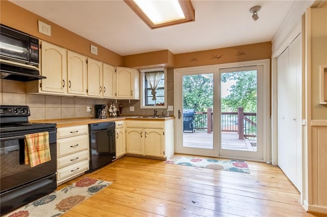 kitchen featuring tasteful backsplash, sink, light hardwood / wood-style flooring, and black appliances