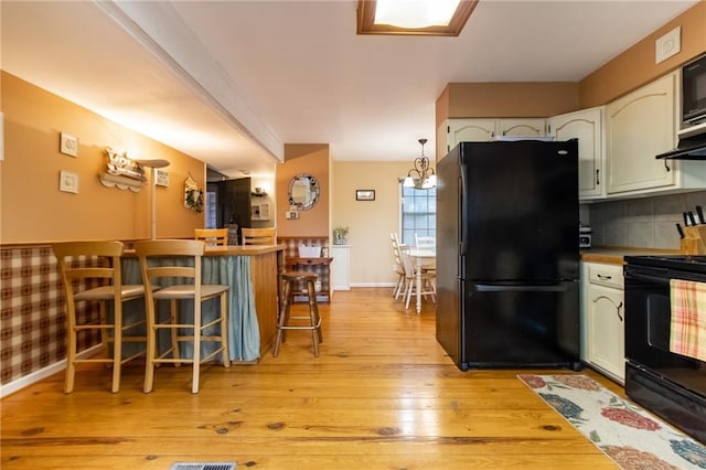 kitchen featuring black appliances, hanging light fixtures, light hardwood / wood-style floors, decorative backsplash, and white cabinets