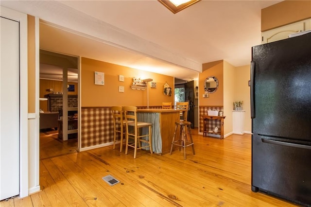 kitchen featuring black refrigerator, light hardwood / wood-style flooring, a breakfast bar area, and beamed ceiling