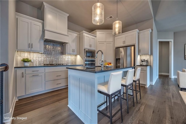 kitchen featuring appliances with stainless steel finishes, decorative light fixtures, an island with sink, and white cabinets