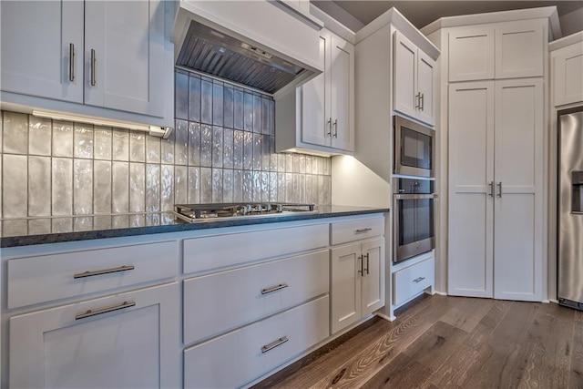 kitchen with white cabinetry, stainless steel appliances, dark hardwood / wood-style floors, tasteful backsplash, and custom exhaust hood