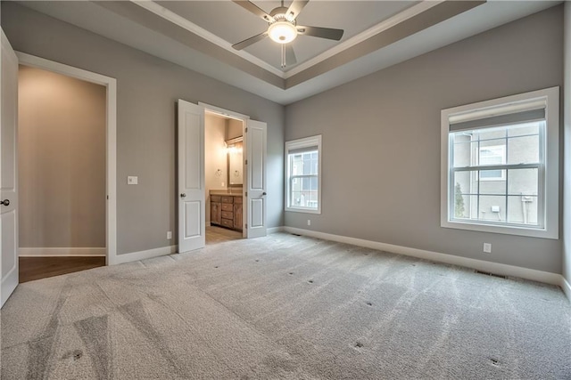 unfurnished bedroom featuring light carpet, ensuite bath, and a tray ceiling