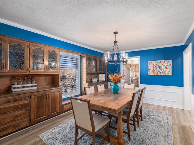 dining space with light wood-style flooring, a textured ceiling, a chandelier, and crown molding