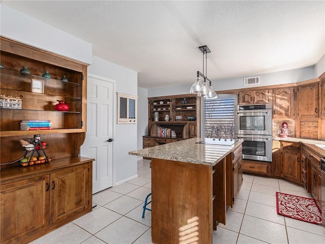 kitchen with light tile patterned floors, visible vents, a kitchen island, light stone counters, and stainless steel double oven