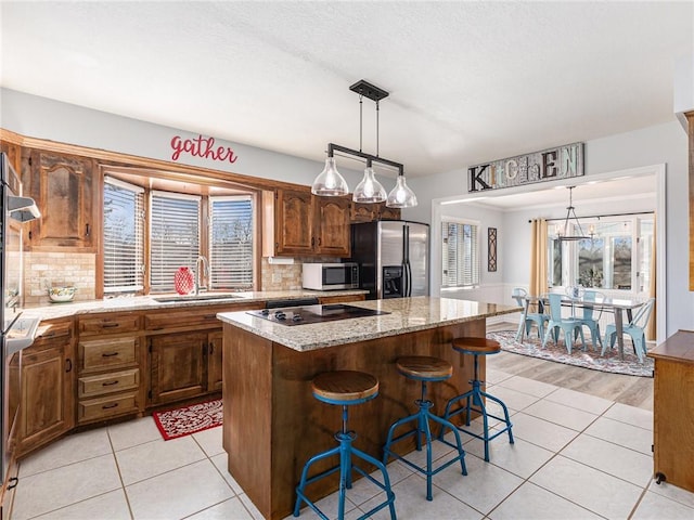 kitchen with light tile patterned floors, appliances with stainless steel finishes, a center island, a kitchen bar, and a sink