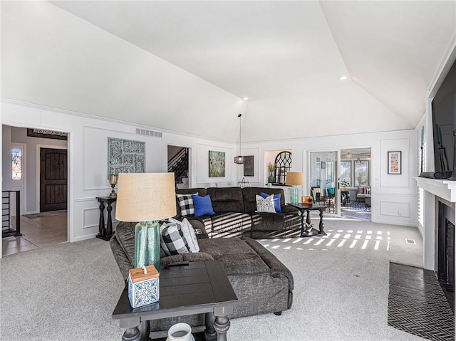 carpeted living area featuring a fireplace with flush hearth, lofted ceiling, visible vents, and a decorative wall