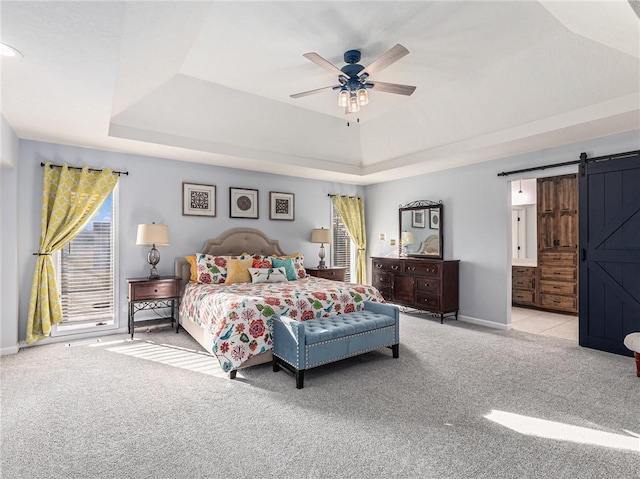 bedroom with ensuite bathroom, a barn door, carpet floors, baseboards, and a tray ceiling