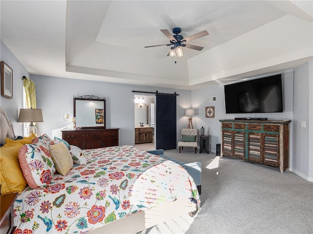 carpeted bedroom with a barn door, baseboards, ensuite bath, ceiling fan, and a tray ceiling