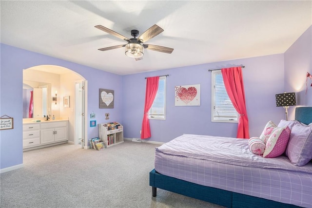 bedroom featuring arched walkways, light colored carpet, ensuite bathroom, ceiling fan, and baseboards