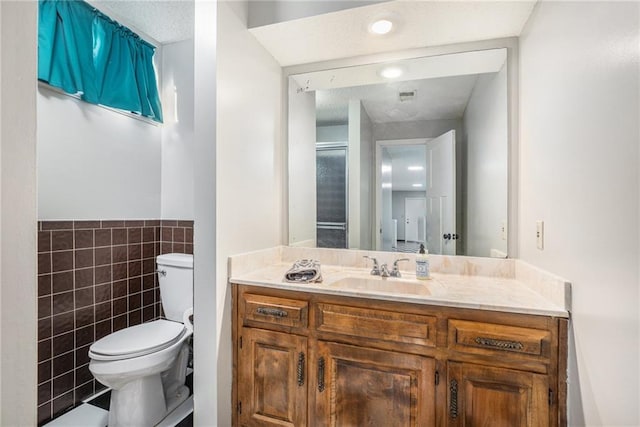 bathroom featuring toilet, a wainscoted wall, visible vents, vanity, and tile walls