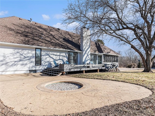 back of house featuring driveway, a shingled roof, a sunroom, a chimney, and a deck