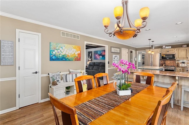 dining room with visible vents, baseboards, ornamental molding, light wood finished floors, and an inviting chandelier