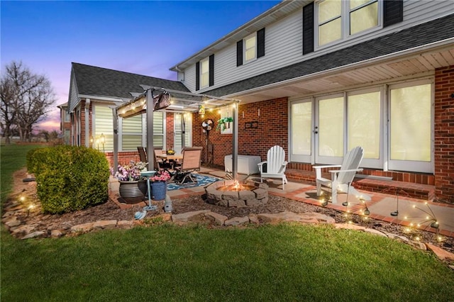 back house at dusk featuring a pergola, a lawn, a patio area, and a fire pit