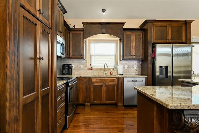 kitchen with light stone counters, dark wood-style flooring, a sink, stainless steel appliances, and tasteful backsplash