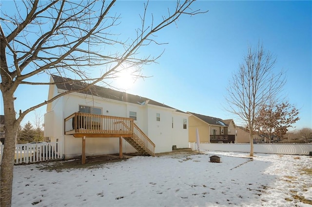 snow covered rear of property with a wooden deck, stairs, a garage, and fence