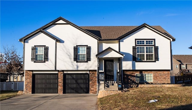 raised ranch with an attached garage, stone siding, and driveway