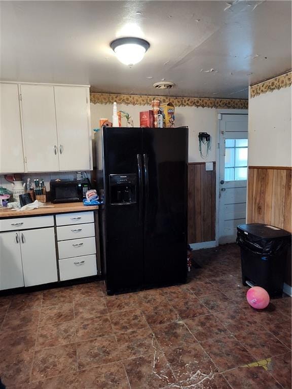 kitchen with black refrigerator with ice dispenser, wooden walls, and white cabinets