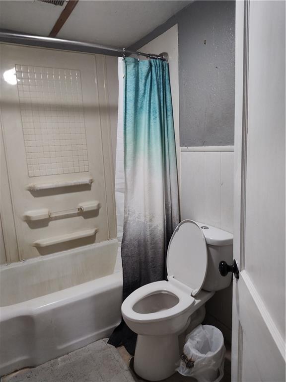 bathroom featuring a wainscoted wall, shower / bathtub combination with curtain, and toilet