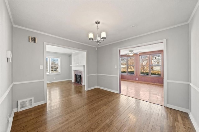 unfurnished living room featuring dark hardwood / wood-style flooring, a fireplace, ornamental molding, and an inviting chandelier