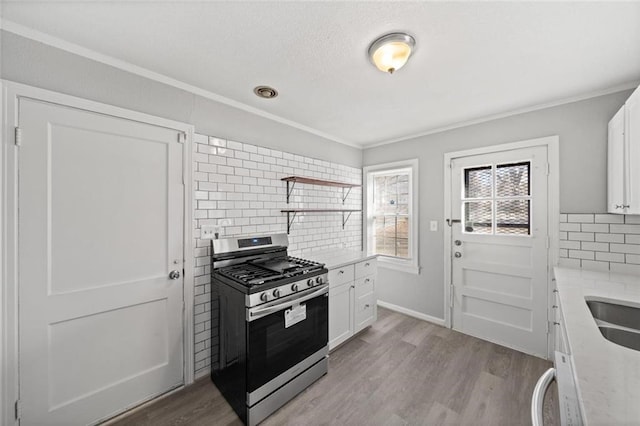 kitchen with light hardwood / wood-style flooring, tasteful backsplash, light stone counters, white cabinets, and gas range