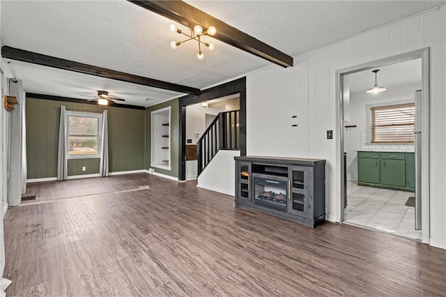 unfurnished living room with ceiling fan, hardwood / wood-style flooring, beamed ceiling, and a textured ceiling