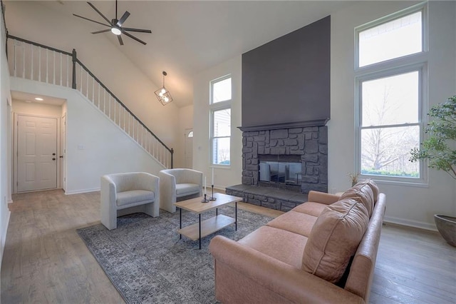 living room with a stone fireplace, light hardwood / wood-style flooring, ceiling fan, and a high ceiling