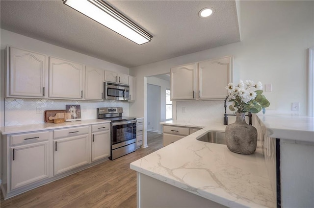 kitchen featuring backsplash, white cabinets, stainless steel appliances, light stone countertops, and light wood-type flooring