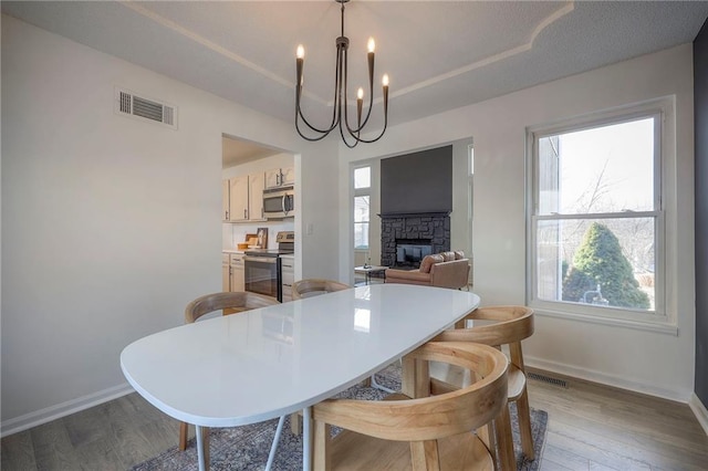 dining space with light hardwood / wood-style flooring, a notable chandelier, a fireplace, and a healthy amount of sunlight