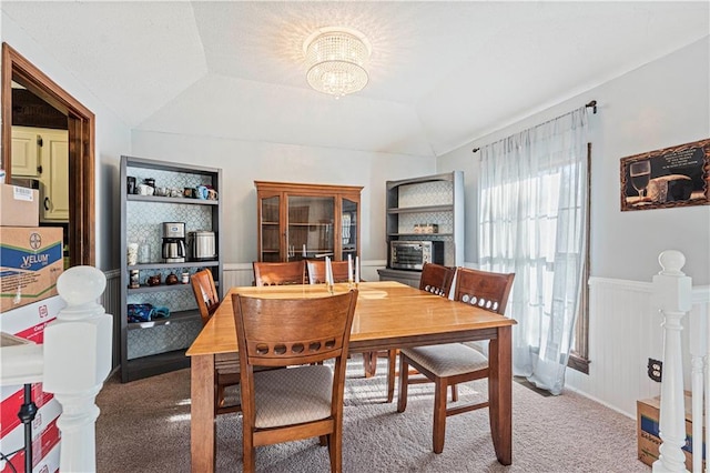 dining room featuring a chandelier, carpet floors, built in features, vaulted ceiling, and wainscoting