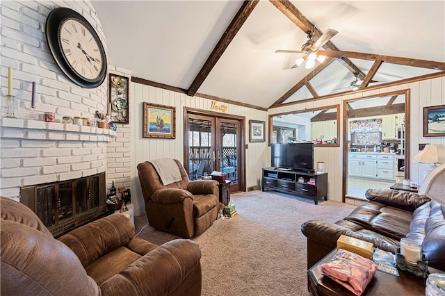 living room featuring french doors, vaulted ceiling with beams, a brick fireplace, carpet flooring, and ceiling fan