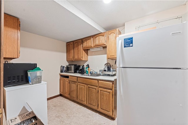 kitchen with light colored carpet, light countertops, freestanding refrigerator, a sink, and baseboards