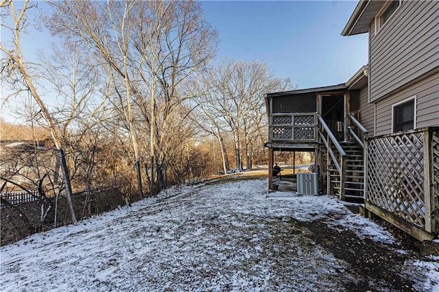 yard covered in snow with a sunroom, central AC, a wooden deck, and stairs