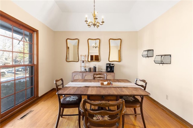 dining area with a tray ceiling, an inviting chandelier, and light hardwood / wood-style flooring