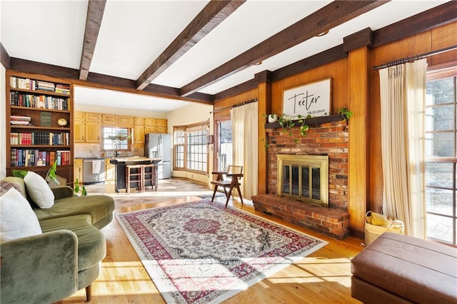 living room featuring beam ceiling, a fireplace, a healthy amount of sunlight, and light wood-type flooring