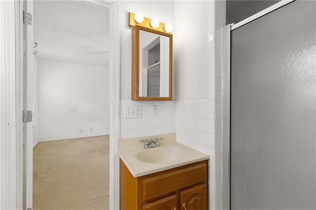 bathroom with walk in shower, vanity, a textured ceiling, and tile walls