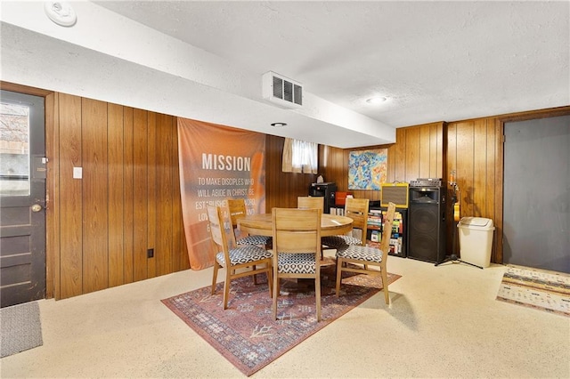 dining space with a textured ceiling, carpet, and wood walls