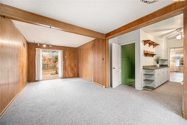 carpeted spare room featuring ceiling fan, beam ceiling, and wood walls