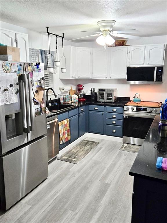 kitchen featuring blue cabinetry, sink, white cabinetry, a textured ceiling, and appliances with stainless steel finishes