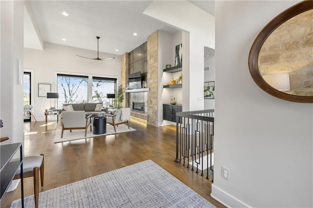 living room with dark wood-type flooring, built in features, ceiling fan, a fireplace, and a high ceiling